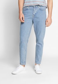 Jeans in denim blu sbiadito con design a gamba dritta, cinque tasche e passanti per cintura, abbinati a sneakers bianche.