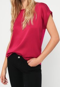 Fuchsia satinblus med korta upprullade ärmar och avslappnad passform, tillsammans med svarta jeans. Slät textur, klassisk rund halsringning.