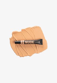 Tubo de corrector de Nudestix sobre una muestra de base beige suave y cremosa. El tubo tiene una tapa negra y letras blancas distintivas para la marca.