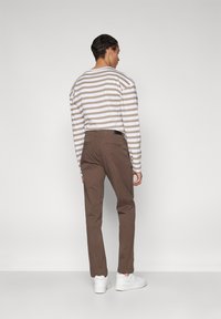 Brown cotton trousers with a relaxed fit, paired with a beige and white striped long-sleeve shirt, and white sneakers.
