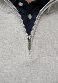 Grå zip-up tröja med en texturerad stickad mönster, med en metallblixtlås med en märkesdragare och en mörkblå shirt under.