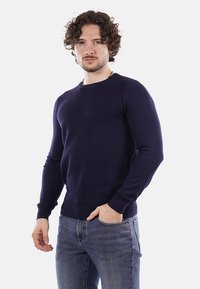 Maglione lavorato a maglia blu navy con scollatura rotonda, polsini e vita a costine. Indossato con jeans in denim chiaro, che mettono in evidenza un design aderente.