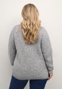 Light gray knitted sweater with a loose fit, textured pattern, dropped shoulders, and ribbed cuffs and hem. Worn over blue denim jeans.