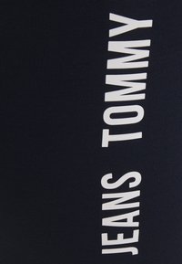 Marinblått tyg med en strukturerad yta, prytt med stora, vita vertikala bokstäver: "JEANS TOMMY." Enkelt och modernt design.