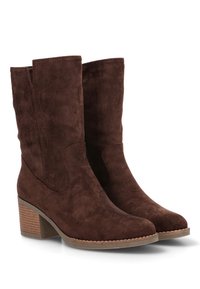 Botas de tobillo de ante marrón con una punta redondeada y un tacón ligeramente apilado. Presenta costuras decorativas a lo largo del borde y una cremallera lateral.