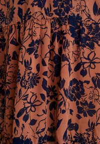 Rostfärgad tyg med marinblå blommönster och samlad söm som skapar mjuka veck och textur.