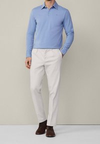 Helleblaues langärmliges Polohemd mit Kragen, kombiniert mit cremefarbenen Hosen und braunen Schnürstiefeln. Einfaches Design, keine sichtbaren Muster.