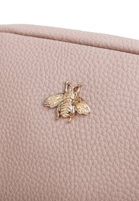 Borsa in pelle beige con texture che presenta un ornamento a forma di ape dorata sul davanti. L'ape ha un design dettagliato delle ali e del corpo.