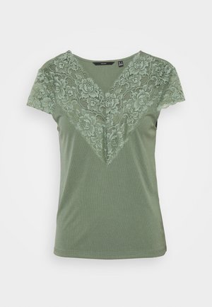 Top vert à manches courtes avec un décolleté en V et un voile de dentelle florale couvrant les épaules et le haut de la poitrine.