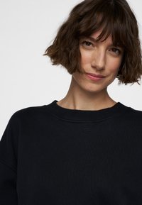 Sudadera negra con cuello redondo, puños acanalados y un detalle texturizado en la parte posterior. Tejido suave con un ajuste ligeramente holgado.