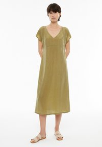 Olivengrünes, knielanges Kleid aus glattem Material. Mit kurzen Ärmeln, einem V-Ausschnitt und einem taillierten Oberteil sowie einem fließenden Rock.