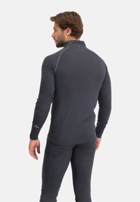 Zwart herenshirt met lange mouwen en een hoge kraag, gemaakt van zachte stof, met grijze stiksels en een logo op de mouw.