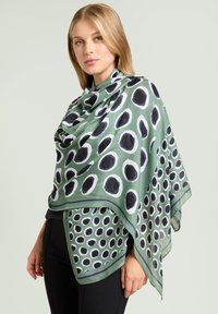 Bufanda verde con un patrón de lunares, con círculos negros y blancos. Tela ligera que cae con estilo, con un borde de contraste.