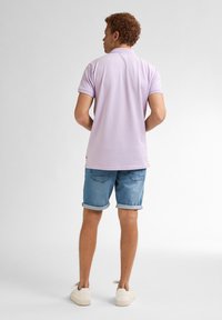 Světle fialová polo košile s klasickým límečkem, spárovaná s ohrnutými denimovými šortkami a bílými teniskami. Hladká textura a volný střih.