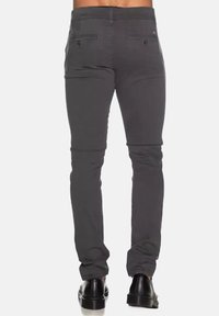 Pantaloni grigi slim-fit con una texture liscia, due tasche posteriori e lunghezza alla caviglia. Abbinati a scarpe nere per un look completo.