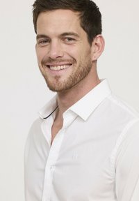 Chemise blanche à boutons avec col ; présente un logo brodé subtil sur la poitrine et un détail en tissu contrasté à l'intérieur du col.