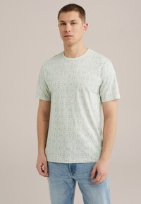 Camiseta de manga corta verde claro con un patrón floral, escote redondo y textura de algodón suave, combinada con vaqueros azules.