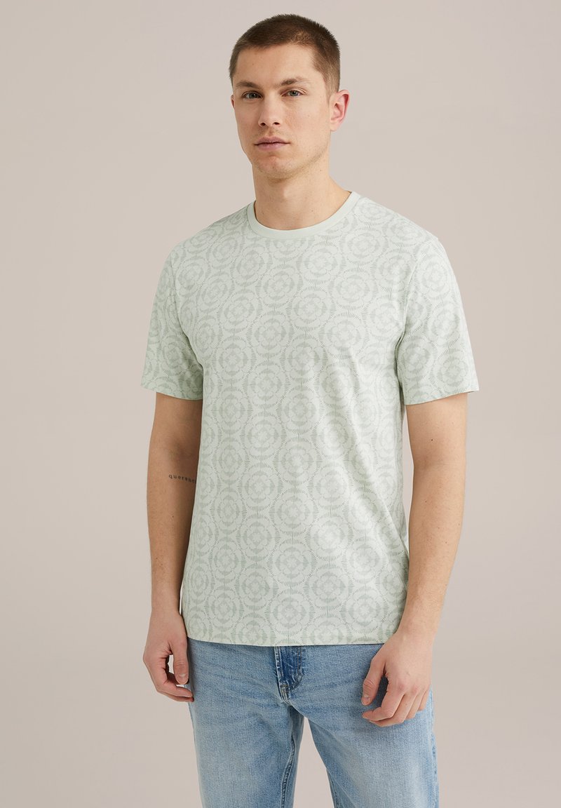 Camiseta de manga corta verde claro con un patrón floral, escote redondo y textura de algodón suave, combinada con vaqueros azules.