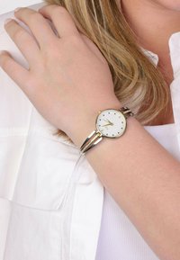 Gold- und Silbermetall Uhr mit einem runden weißen Zifferblatt, minimalistischen Stundenmarkierungen und einem zweifarbigen Armband mit Kristallakzenten.