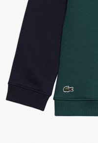 Sweatshirt a blocchi di colore in tessuto blu navy scuro e verde bosco, con polsini a coste e un piccolo logo di coccodrillo ricamato.