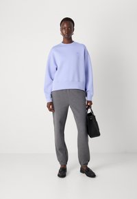 Lys lilla genser med avslappet passform og ribbede mansjetter, kombinert med grå joggebukser. Svart håndveske og loafers fullfører antrekket.