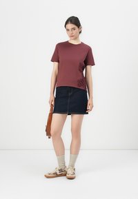Bordeaux kortermet t-skjorte med blomster mønster på siden, parret med en mørk denim skjørt og beige sokker. Brukt med joggesko og en håndveske.