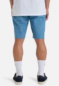 Blauwe, knielange shorts van een gestructureerde stof. Heeft een relaxte pasvorm en wordt gecombineerd met witte geribbelde sokken en marineblauwe schoenen.