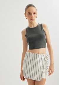 Grå ribbet crop top parret med en hvid omslagsskjørt med sorte lodrette striber og en sideknude. Blødt stof med glat tekstur.