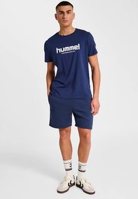 Marinblå sport-T-shirt med vit text, kombinerad med matchande shorts. Har en avslappnad passform och mjuk textur. Komplett med vita och svart randiga strumpor.