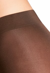 Collants bruns transparents avec une texture lisse et une taille côtelée, montrant des variations de couleur subtiles et un gros plan du tissu.