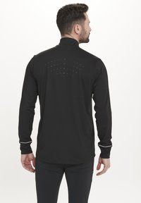 Sort langærmet atletisk skjorte med høj krave, der har et struktureret rygdesign med små prikker og kontrasterende ærmer.