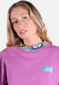 Sweatshirt violet avec un col en tricot à motifs bleu, jaune et blanc. Comprend une étiquette logo Oxbow bleue à l'avant.