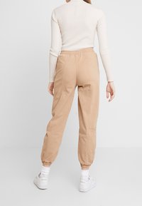 Beżowe spodnie dresowe z elastycznym paskiem w talii i ściągaczami, z gładkim wykończeniem i detalami na bocznych szwach; w zestawieniu z białymi sneakersami.