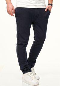 Navy Sweatpants aus weichem Stoff, mit slim-fit Schnitt, Seitentaschen und gerippten Bündchen, kombiniert mit weißen Sneakers.