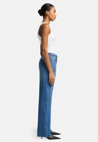 Jeans in denim azzurro chiaro con vestibilità dritta, vita alta e orlo sfilacciato, abbinati a tacchi neri a punta e una canotta bianca.