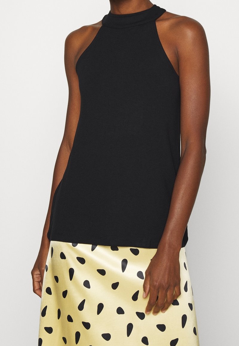 Haut sans manches noir avec un col montant, fabriqué en tissu doux. Associé à une jupe dorée ornée de motifs en forme de goutte noirs.