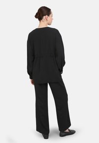 Black relaxed-fit top with long sleeves and elastic waist, paired with loose black pants. Soft texture and minimal design.