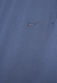 Polo shirt Nike albastru, realizat dintr-un material texturat. Prezintă un mic logo negru în zona stângă a pieptului. Designul include un guler clasic și o plăcuță cu nasturi.