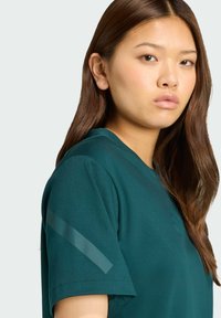 Tyrkysové bavlnené tričko s krátkymi rukávmi, ponúkajúce jemný pruhovaný vzor na pleciach a okrúhly výstrih, vystavené na svetlom pozadí.