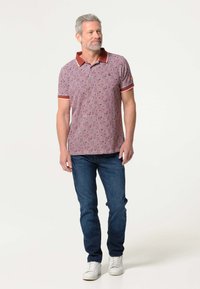 Korte mouwen polo in het rood met een geometrisch patroon, contrasterende kraag en geribbelde accenten. Gecombineerd met blauwe jeans en witte sneakers.