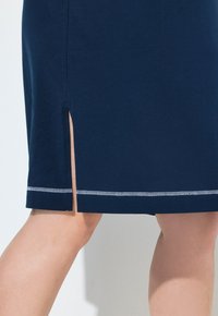 Granatowa sukienka bawełniana z bocznym rozcięciem i kontrastującym białym przeszyciem wzdłuż dołu. Gładka tekstura, długość do kolan.