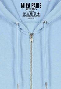 Felpa leggera blu, 100% cotone. Presenta una chiusura frontale con zip argentata, lacci e un'interior texture morbida. Istruzioni per la cura incluse.