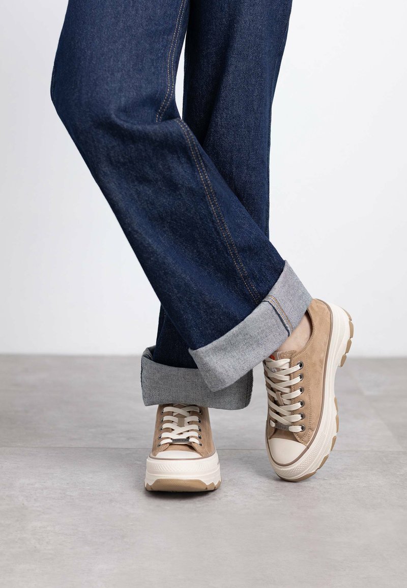 Zapatillas de ante beige con suelas y cordones de goma blanca, combinadas con jeans de mezclilla azul oscuro con los dobladillos doblados.