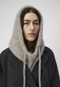 Grijze wollen jas met een lichtbeige, gebreide, oversized capuchon met een pluizige textuur en trekkoorden aan de voorkant.