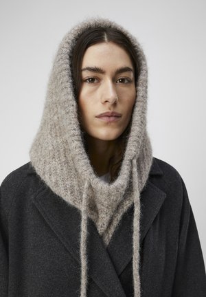 Harmaa villakangastakki, jossa on vaaleanbeige, neulottu, ylisuurikokoinen huppu, jossa pörröinen tekstuuri ja edessä kiristysnyörit.