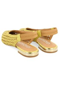 Sandalias trenzadas amarillas con una suela plana acentuada en dorado, que cuentan con correas elásticas y un parte superior texturizada para la transpirabilidad.