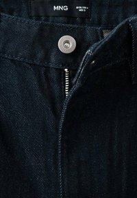 Tummafarkut hopeisella vetoketjulla ja metallisella napilla. Niissä on tummansininen väri, hieno tekstuuri ja MNG-merkki vyötäröllä.