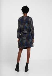 Krátké šaty s dlouhým rukávem z tmavé látky s modro-hnědým květinovým vzorem, s přiléhavým pasem a nařasenou sukní nad kolena.