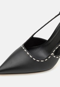 Scarpa slingback in pelle nera con punta affusolata e dettagli bianchi cuciti lungo l'apertura. Texture liscia e design minimalista.