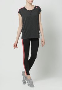 Camiseta deportiva gris de manga corta, con detalles en rosa en los hombros, combinada con leggings negros con rayas rosas y zapatillas grises.
